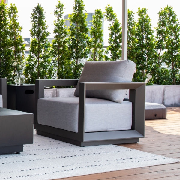 Modern outdoor furniture set with gray cushions on a wooden deck with green trees in the background