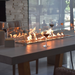     Elementi Workshop Dining Rectangular Concrete Fire Pit Table Close Up Look With Flame On And Wine Glasses On The Sides Of The Windscreen